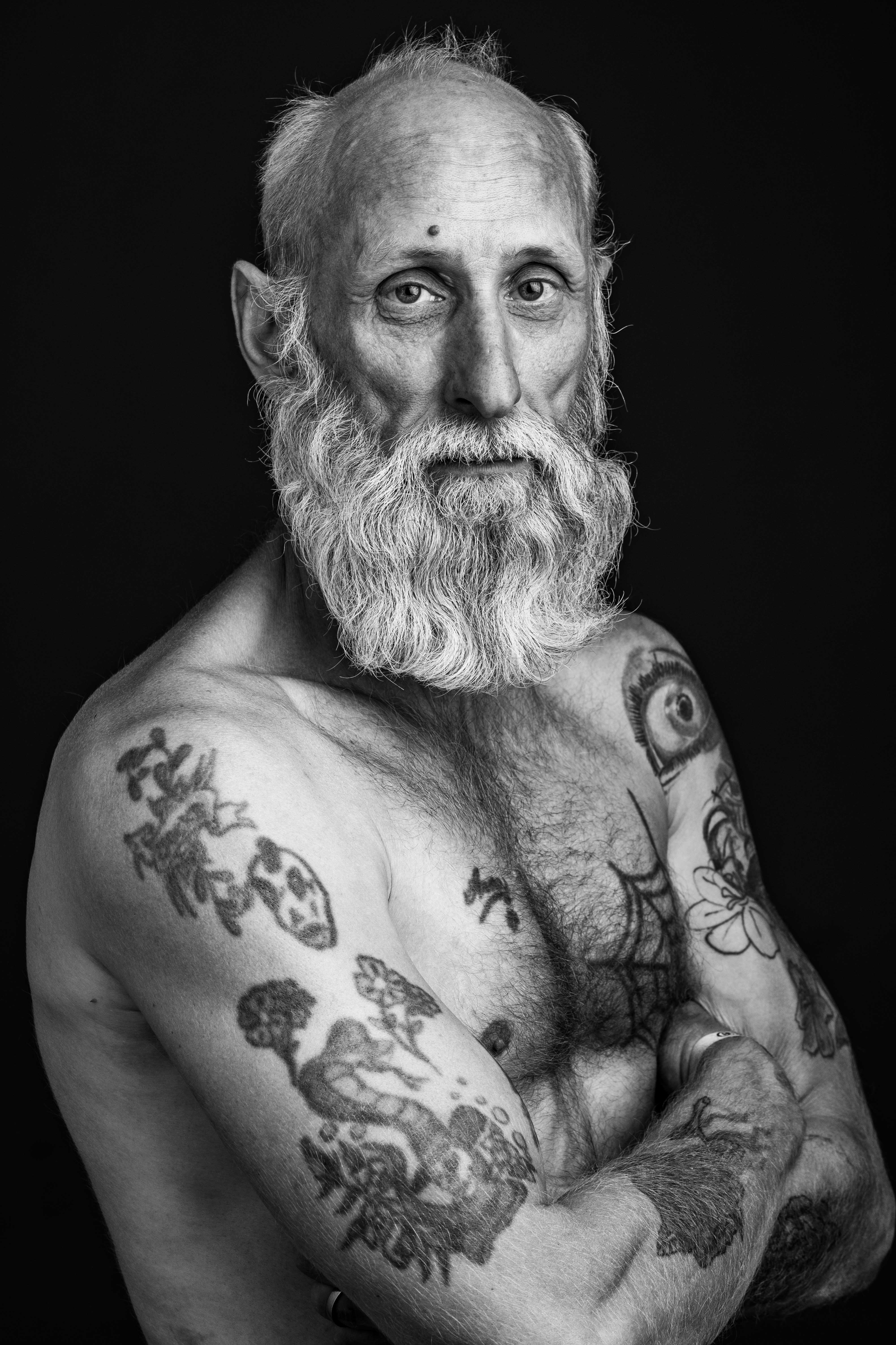 Porträtt av tatuerad gråhårig man med bar överkropp